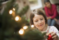 Girl placing bauble on Christmas tree — Stock Photo