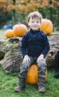 Menino sentado em uma grande abóbora laranja — Fotografia de Stock