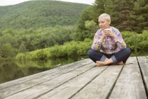 Femme assise sur un quai avec une tasse de café — Photo de stock