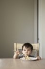 Kleiner Junge sitzt auf einem Stuhl an einem Tisch — Stockfoto