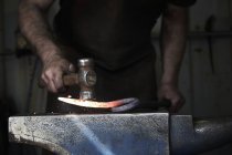 Herrero dando forma a un pedazo caliente de hierro - foto de stock