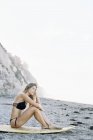 Frau im Bikini sitzt auf ihrem Surfbrett — Stockfoto