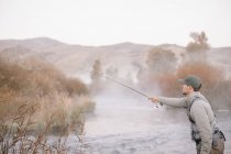 Hombre pescando con mosca desde una orilla del río . - foto de stock