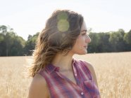 Mujer de pie en un campo de trigo maduro alto - foto de stock