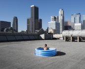 Людина в надувному басейні на міському даху — стокове фото