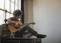 Hombre tocando la guitarra sentado junto a una ventana . - foto de stock