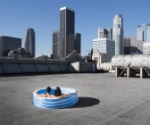 Casal na piscina inflável em um telhado da cidade — Fotografia de Stock