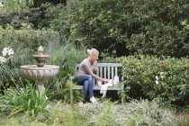 Donna seduta su una panchina di legno in un giardino — Foto stock