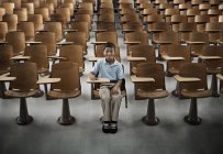 Boy sitting in a hall of empty desks. — Stock Photo