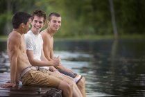 Meninos sentados no molhe ao lado do lago — Fotografia de Stock