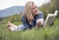 Frau liegt im Gras und liest ein Buch — Stockfoto