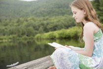 Menina lendo por um lago — Fotografia de Stock