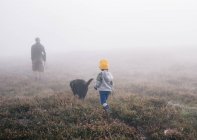 Adult and a child with a dog in autumn mist. — Stock Photo