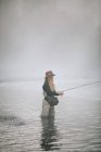 Woman flyfishing in waders in thigh deep water. — Stock Photo