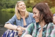Two women laughing while sitting near water — Stock Photo