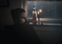 Hombre sentado en la oscuridad junto a una ventana - foto de stock