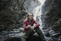 Uomo seduto su una roccia vicino a una cascata — Foto stock