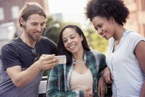 Mann und zwei Frauen schauen auf ein Smartphone — Stockfoto