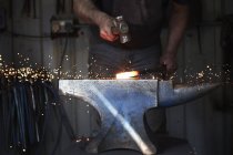 Herrero dando forma a un pedazo caliente de hierro - foto de stock