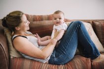 Woman lying on a sofa with baby girl. — Stock Photo