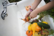 Mädchen wäscht Gemüse unter einem Wasserhahn. — Stockfoto