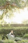 Жінка сидить в саду, читаючи — стокове фото