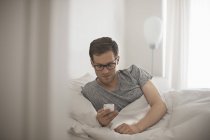 Чоловік лежить у ліжку перевіряє телефон — стокове фото