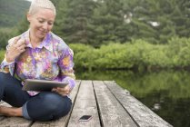 Donna seduta sul molo utilizzando tablet — Foto stock