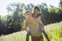 Man giving woman a piggyback on meadow — Stock Photo