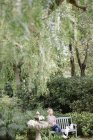 Donna seduta su una panchina di legno in un giardino — Foto stock