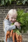 Fille tenant un grand bouquet de carottes . — Photo de stock