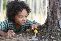Kind legt sich hin und inspiziert Pilz — Stockfoto