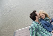 Hombre y mujer sentados en un embarcadero junto a un lago . - foto de stock
