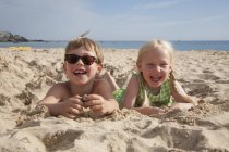 Niño y niña acostados en la arena - foto de stock