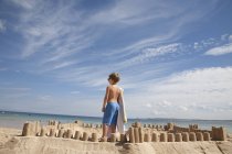 Boy standing beside a sandcastle — Stock Photo