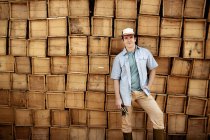 Granjero frente a una pared de cajas de madera - foto de stock
