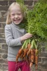 Girl holding a large bunch of carrots. — Stock Photo
