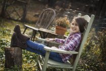 Дівчина сидить у дерев'яному стільці в саду — стокове фото
