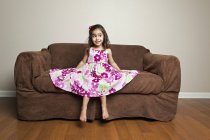Mädchen sitzt auf einem braunen Sofa. — Stockfoto