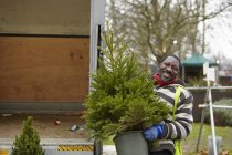 Uomo che porta un pino in un centro giardino — Foto stock