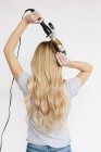 Woman with blond hair using curling tongs — Stock Photo