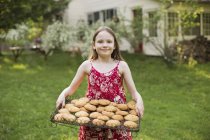 Menina segurando bandeja de biscoitos cozidos frescos — Fotografia de Stock