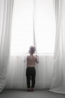 Child looking out through net curtains — Stock Photo