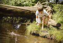 Niño arrodillado por la orilla del río - foto de stock