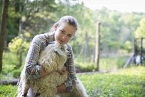 Teenager kneeling and putting arms around goat — Stock Photo