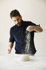 Baker sprinkling flour over bread dough. — Stock Photo