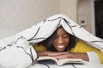 Девушка чтение книги под одеялом — стоковое фото