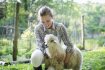 Teenager kneeling and putting arms around goat — Stock Photo