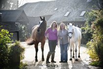 Dos mujeres de pie con caballos - foto de stock