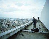 Fotógrafo em pé em um telhado em uma cidade — Fotografia de Stock